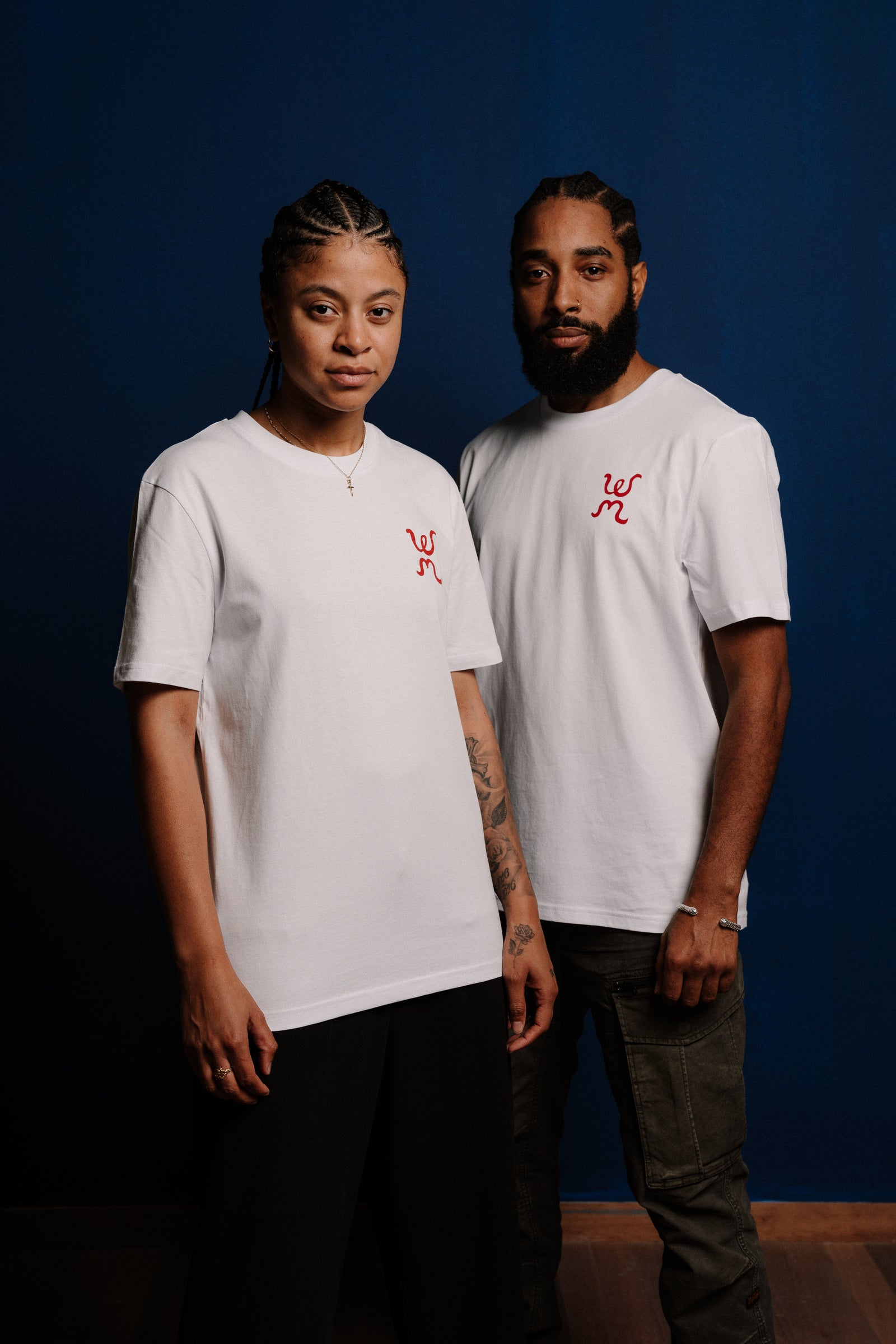 Two people wearing white t-shirts with a red logo against a dark blue background