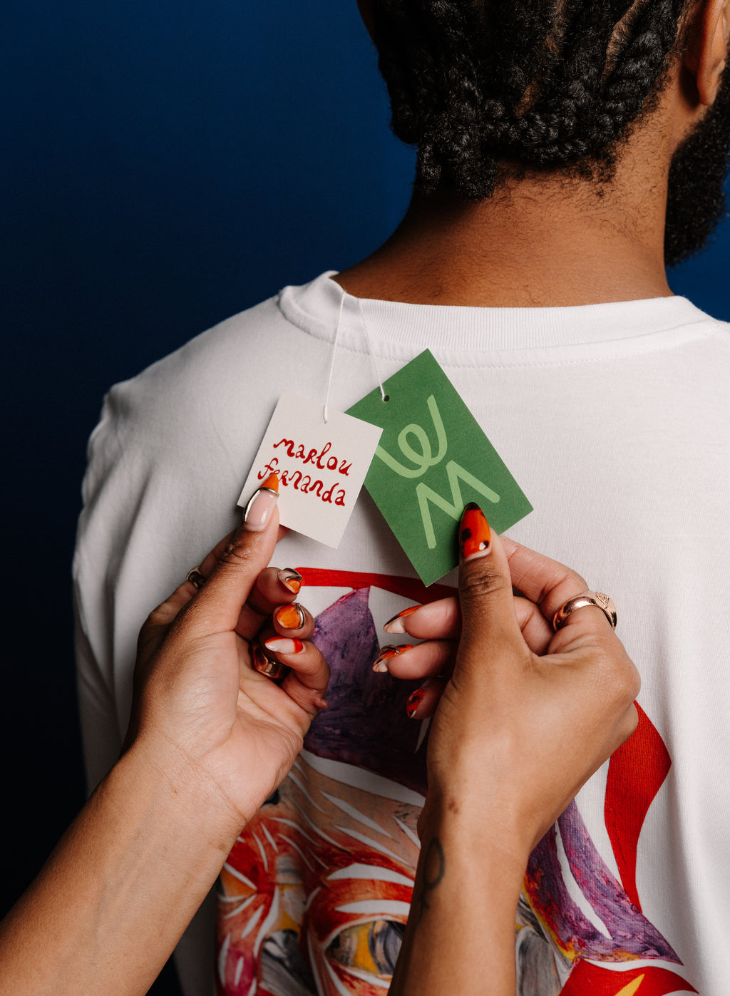 Person holding clothing tags with text on a white shirt against a dark background