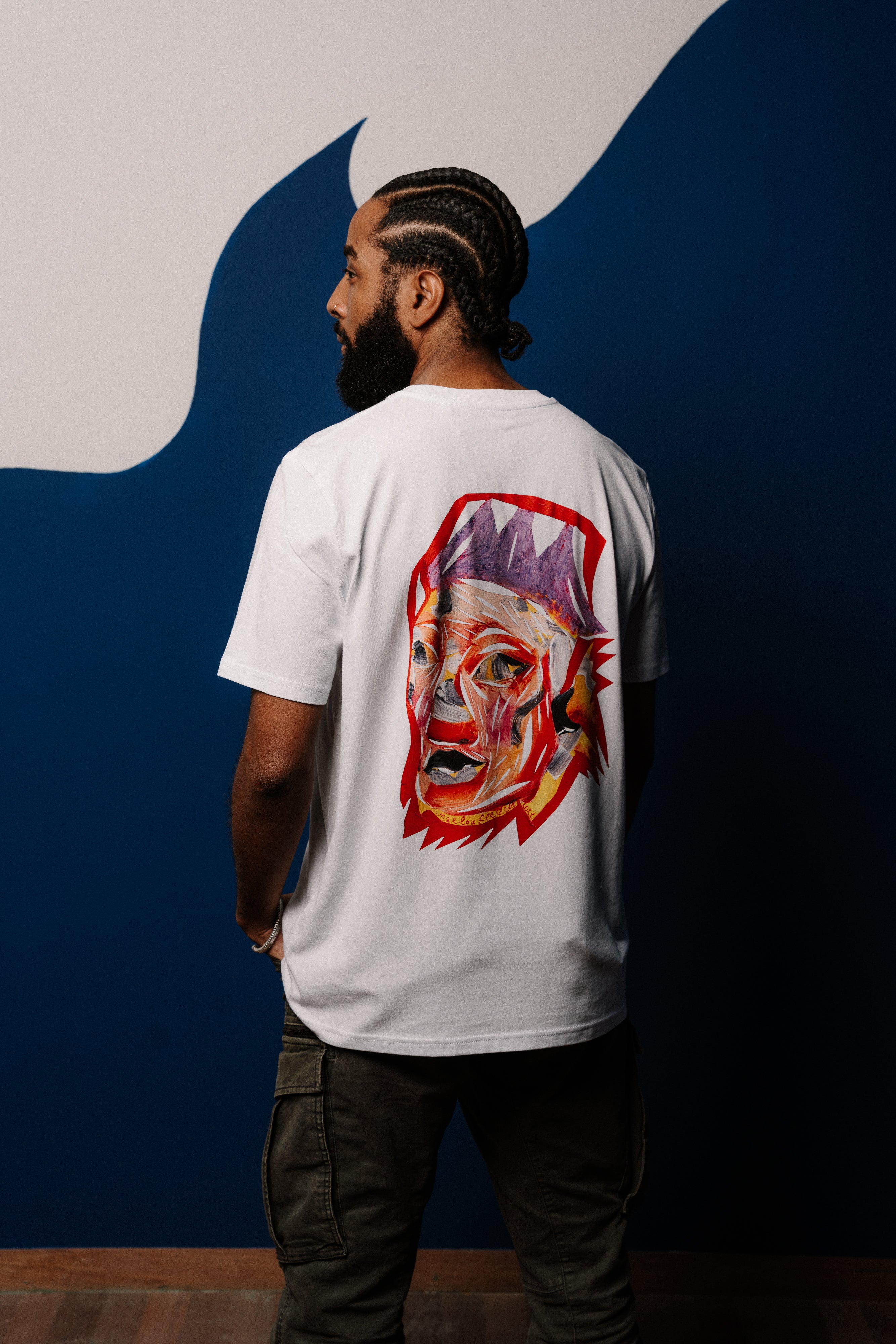 Person wearing a white t-shirt with a colorful graphic on the back against a blue and gray wall.